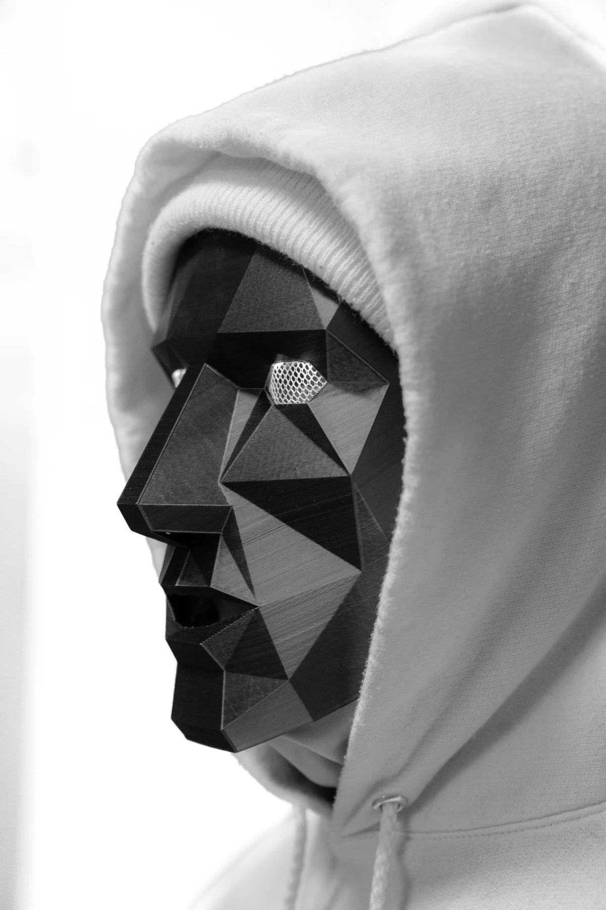 NoFace standing in a white hoodie under angular shadows